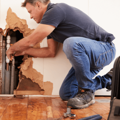 Plumber fixing a burst water pipe in the wall